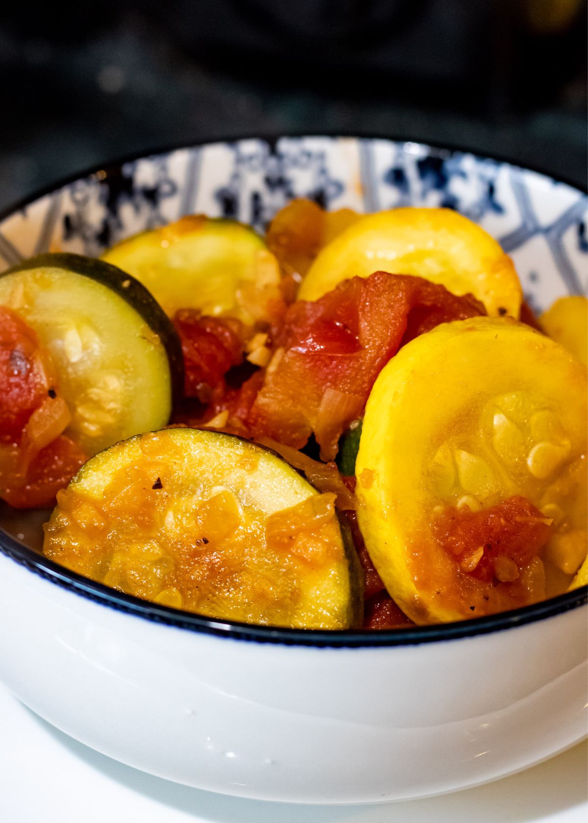 Close up of a bowl with zucchini, squash and tomatoes cooked together.