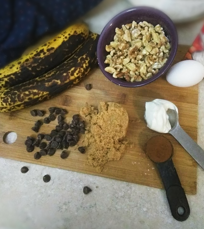 banana nut scone ingredients with ripe bananas, bowl of walnuts, chocolate chips, brown sugar, egg, spoonful of cinnamon and sour cream