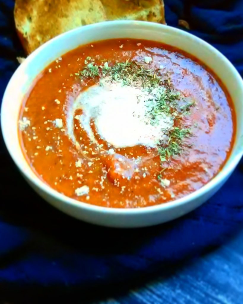 roasted red pepper, tomato, and carrot soup in white bowl with cream and herbs on top