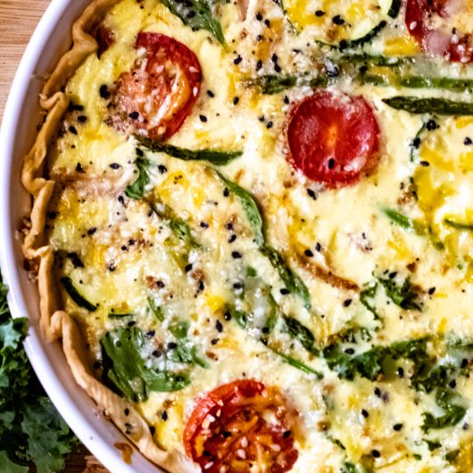 quiche baked with sliced tomatoes, squash, kale, spinach, asparagus, and cheeses.