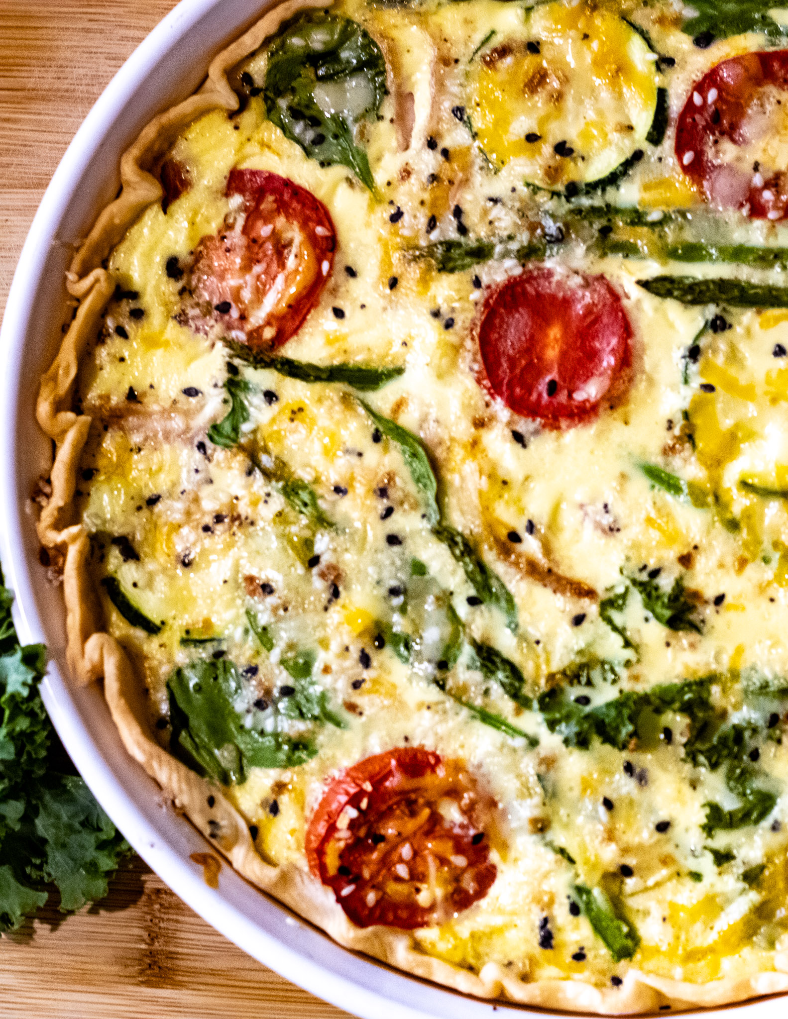 quiche baked with sliced tomatoes, squash, kale, spinach, asparagus, and cheeses.