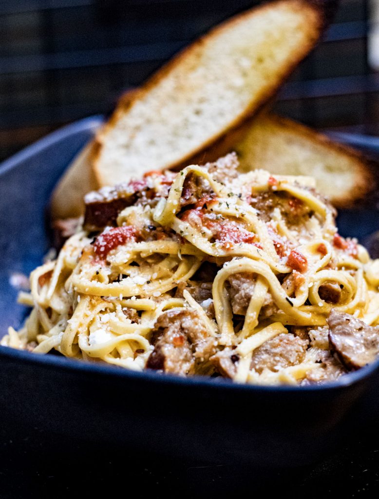 Bowl of sausage and pepper pasta with two pieces of crusty bread.