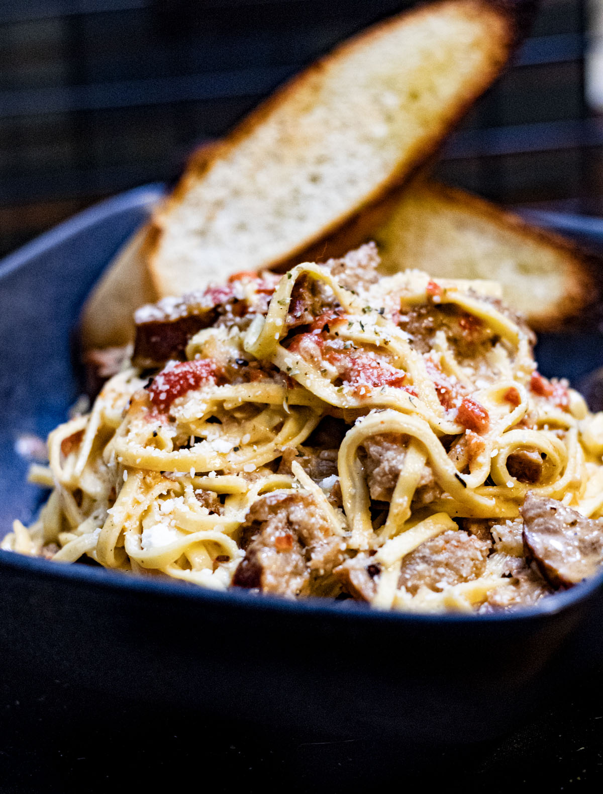 Bowl of sausage and pepper pasta with two pieces of crusty bread.