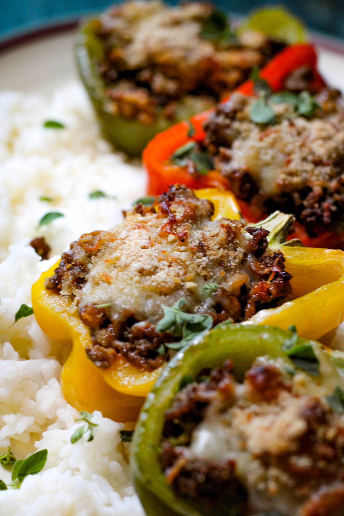 4 stuffed peppers over white rice with different color bell peppers.