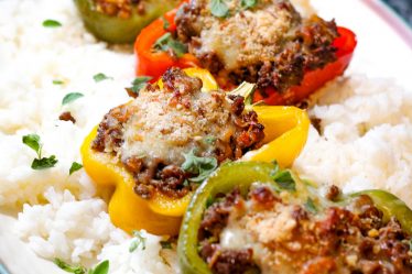 Large platter with halved bell peppers in a variety of colors filled with recipe and served over white rice.