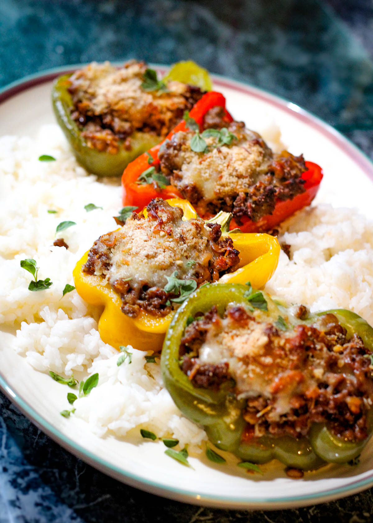 Large platter with halved bell peppers in a variety of colors filled with recipe and served over white rice.