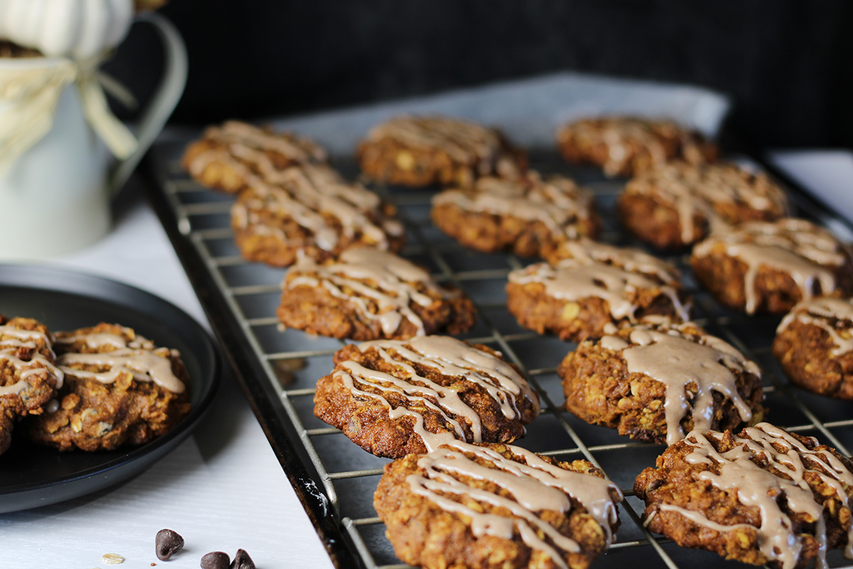 Pumpkin oatmeal cookies on a wire rack drizzled with icing with two more cookies on a plate nearby.