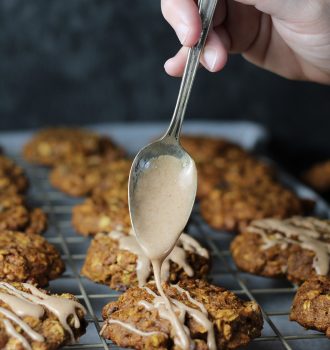 Cinnamon maple icing being drizzled over a tray of pumpkin oatmeal cookies.