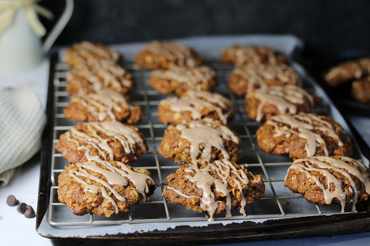 Pumpkin oat cookies with icing drizzled on top on a wire rack.