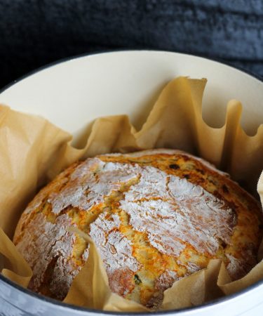 Jalapeno cheddar bacon bread in a parchment lined Dutch oven.