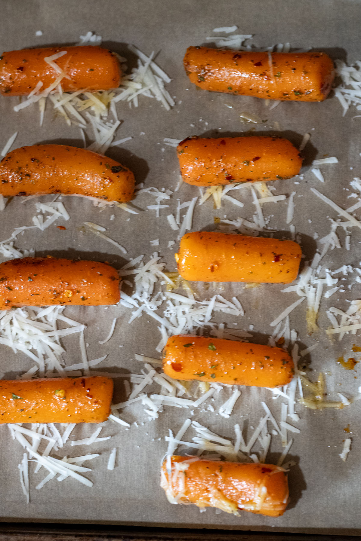 Cooked and seasoned carrots on a parchment lined sheet pan with cheese.
